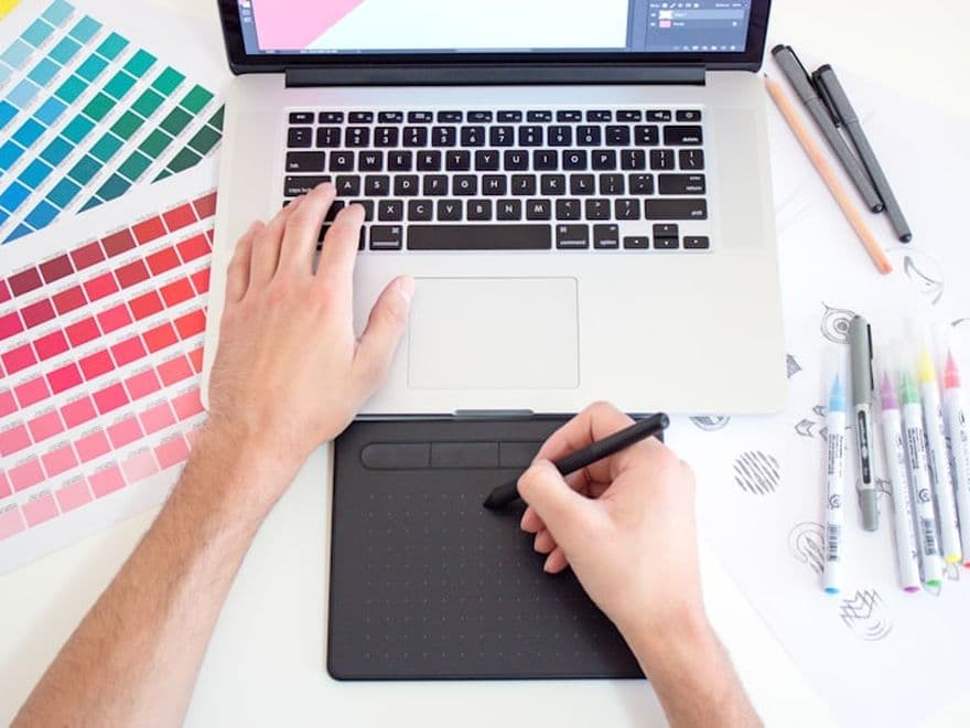 Graphiste dessinant un logo sur une tablette, nuancier à côté