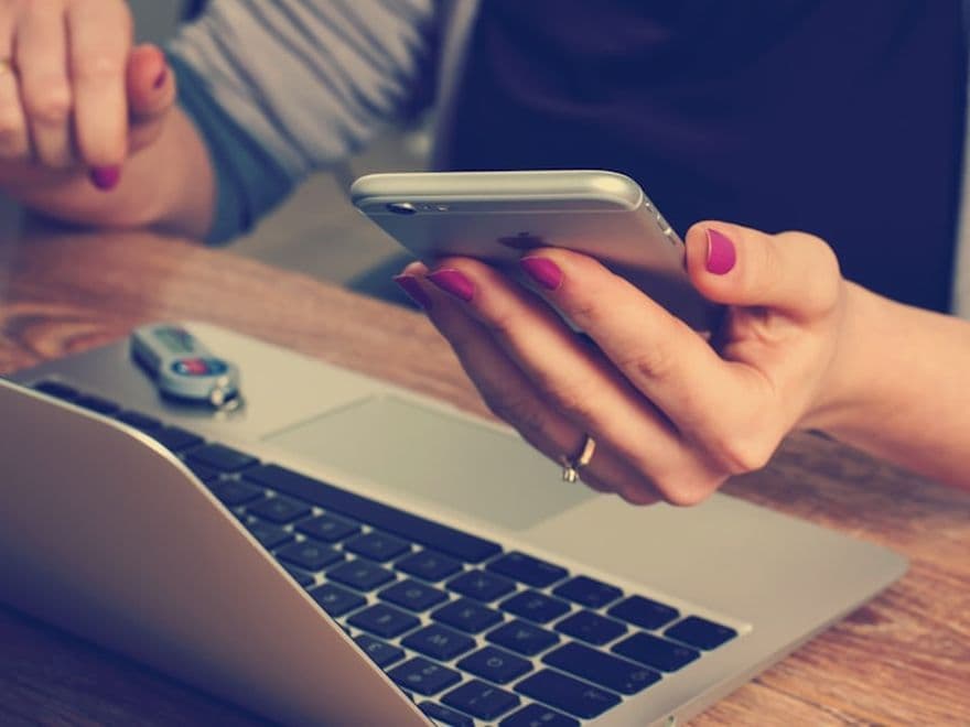 Personne effectuant une recherche sur son téléphone à côté d'un ordinateur